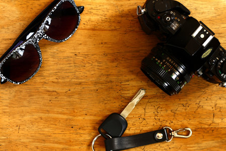 Photo of a manual camera, car key and sunglasses on a table inside a bedroom