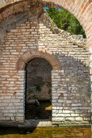 Sunlit ancient limestone archway at the edge of a reflective water channel within the archaeological...