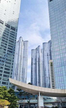 A group of modern skyscrapers with glass facades reaching towards a blue sky with scattered clouds, creating an urban architectural landscapeの写真素材