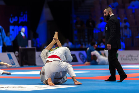 ABU DHABI, UAE - APRIL 19, 2016: ABU DHABI WORLD PROFESSIONAL JIU-JITSU CHAMPIONSHIP 2016 in the IPIC ARENA. Men in white kimonos fighting in the parterre. Referee is near.のeditorial素材