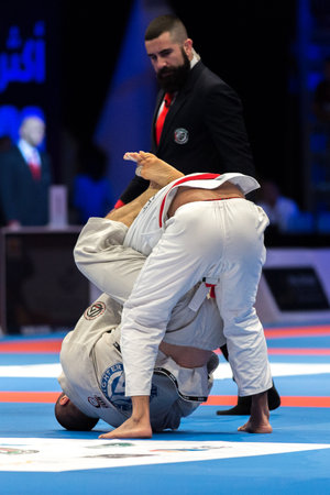 ABU DHABI, UAE - APRIL 19, 2016: ABU DHABI WORLD PROFESSIONAL JIU-JITSU CHAMPIONSHIP 2016 in the IPIC ARENA. Men in white kimonos fighting on the mat. Referee following for them.のeditorial素材