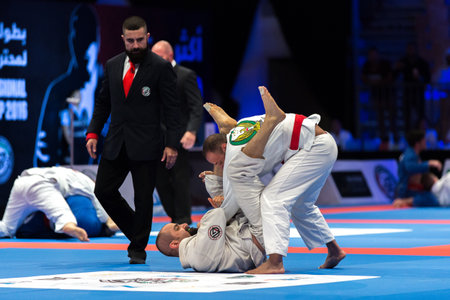ABU DHABI, UAE - APRIL 19, 2016: ABU DHABI WORLD PROFESSIONAL JIU-JITSU CHAMPIONSHIP 2016 in the IPIC ARENA. Referee following for the men in white kimonos on the mat.のeditorial素材