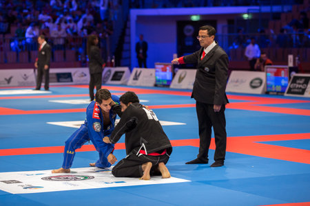 ABU DHABI, UAE - APRIL 19, 2016: ABU DHABI WORLD PROFESSIONAL JIU-JITSU CHAMPIONSHIP 2016 in the IPIC ARENA. Fighters men in blue and black kimonos are fighting. The referee gives a point for fighter in black kimono.のeditorial素材