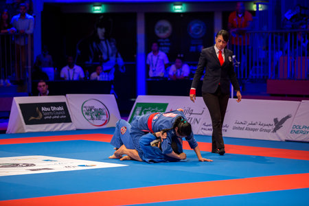 ABU DHABI, UAE - APRIL 19, 2016: ABU DHABI WORLD PROFESSIONAL JIU-JITSU CHAMPIONSHIP 2016 in the IPIC ARENA. Referee following women in blue kimonos fighting in the parterre.のeditorial素材