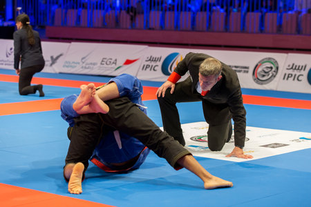 ABU DHABI, UAE - APRIL 19, 2016: ABU DHABI WORLD PROFESSIONAL JIU-JITSU CHAMPIONSHIP 2016 in the IPIC ARENA. Referee following fighters in kimonos fighting in the parterre.のeditorial素材