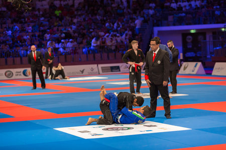 ABU DHABI, UAE - APRIL 19, 2016: ABU DHABI WORLD PROFESSIONAL JIU-JITSU CHAMPIONSHIP 2016 in the IPIC ARENA. Fighters on the mat. Judge stands near.のeditorial素材