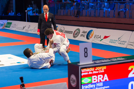 ABU DHABI, UAE - APRIL 19, 2016: ABU DHABI WORLD PROFESSIONAL JIU-JITSU CHAMPIONSHIP 2016 in the IPIC ARENA. Fighters with brown belts on the mat. Referee is next to them.のeditorial素材