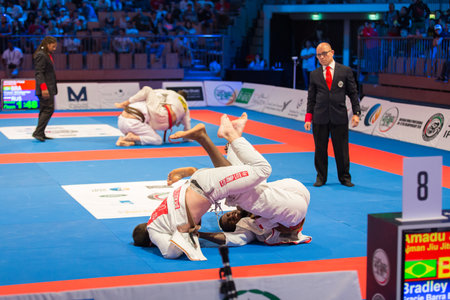 ABU DHABI, UAE - APRIL 19, 2016: ABU DHABI WORLD PROFESSIONAL JIU-JITSU CHAMPIONSHIP 2016 in the IPIC ARENA. Fighters with brown belts on the mat fight aggressivily. Referee following them.のeditorial素材