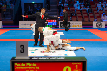 ABU DHABI, UAE - APRIL 19, 2016: ABU DHABI WORLD PROFESSIONAL JIU-JITSU CHAMPIONSHIP 2016 in the IPIC ARENA. Male fighters black belts on the mat. Referee stops fighting.のeditorial素材