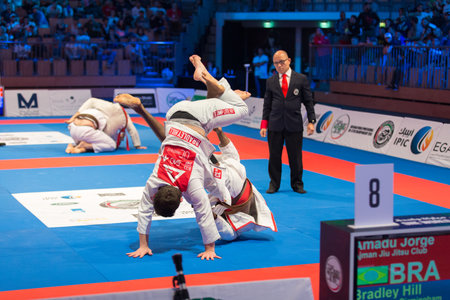 ABU DHABI, UAE - APRIL 19, 2016: ABU DHABI WORLD PROFESSIONAL JIU-JITSU CHAMPIONSHIP 2016 in the IPIC ARENA. Fighters with brown belts on the mat fight aggressivily. Referee following them.のeditorial素材