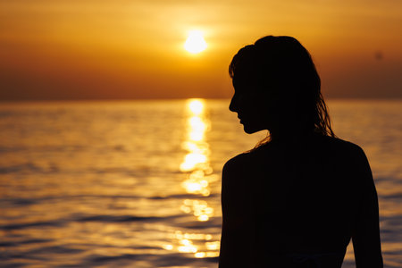 Silhouette of a girls profile against the background of the sea at sunset.の写真素材