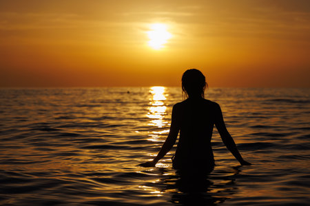 Silhouette of a girl going into the sea at sunset.の写真素材