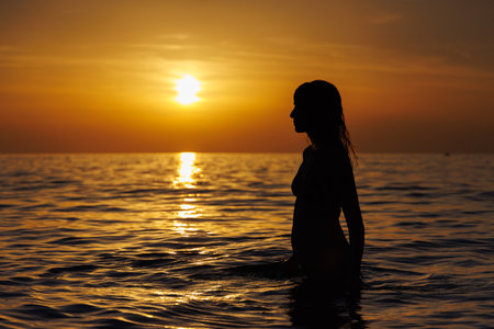 Silhouette of a girl looking at the sun in the sea at sunset.の写真素材