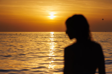 Silhouette of a girls profile in out of focus against the background of the sea at sunset.の写真素材