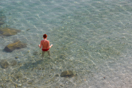 A woman stands waist-deep in the calm sea. Shes wearing a red swimsuit.の写真素材