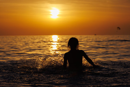 Silhouette of a girl in the spray of the sea at sunset.の写真素材
