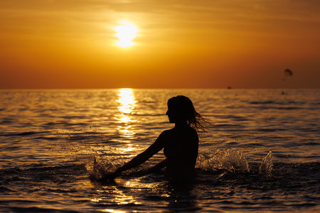 Silhouette of a girl playing with water in the sea at sunset.の写真素材