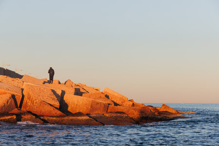 A person with their back to us on the breakwater at sunset.の写真素材