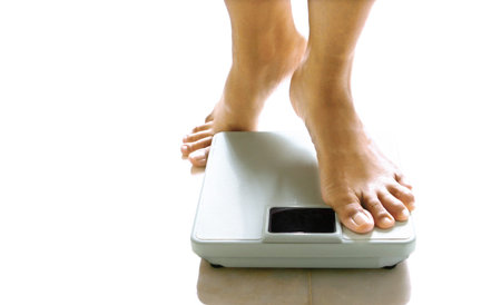 Pair of feminine feet about to stand on a weighing scale.