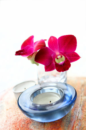 Red oriental orchid in glass vase with aromatherapy candle, part of health and beauty spa setting.の写真素材