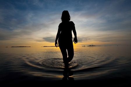 Silhouette of woman walking in shallow water during sunriseの写真素材