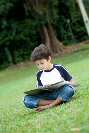 Young boy enjoying his reading book in outdoor parkの写真素材