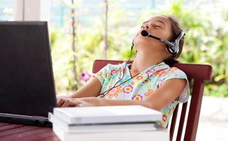 Young girl listening to headphone while on laptop computer, resting her head on chair.の写真素材