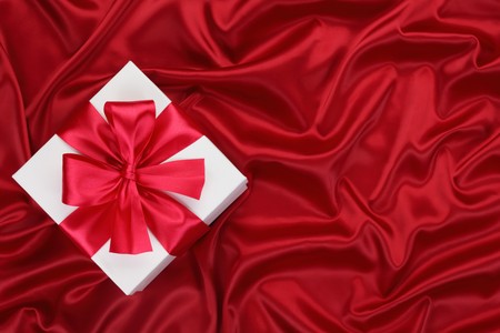 Gift with ribbon and bow on the red silk background.の写真素材