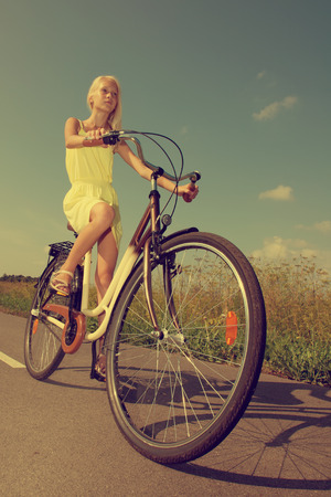 Young girl in yellow dress riding a retro style bike の写真素材