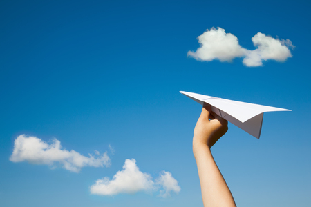 Paper plane in child hand on blue sky and clouds background. (With space for text.)の写真素材