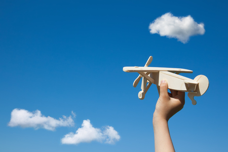 Wooden plane in child hand on the blue sky and clouds background. ( With space for text.)の写真素材