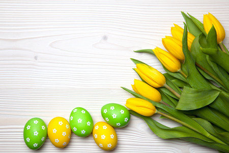 Easter eggs and yellow tulips on white wooden background.の写真素材