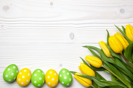 Easter eggs and yellow tulips on white wooden background.の写真素材