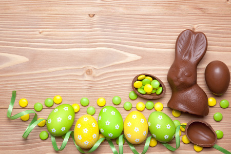 Easter eggs, chocolate easter bunny, candies and ribbon on wooden background.の写真素材