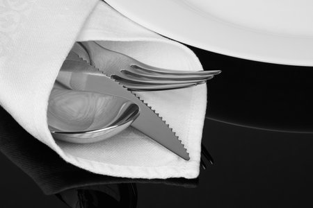 Close-up of knife, fork and spoon with white linen serviette on the black background.の写真素材