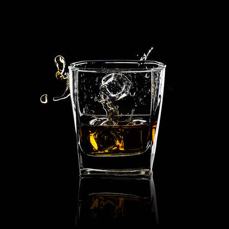 Glass of splashing whiskey isolated on blackの写真素材