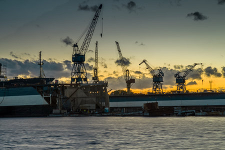 Harbor scene with large cargo ships, cranes, and industrial infrastructure at dusk or dawn. Busy...