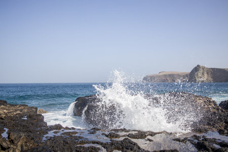 Waves crashing against a rocky shoreline. Dramatic coastal scene with powerful waves and dark...