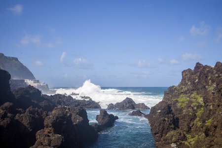 Visitors enjoy the stunning natural beauty of Madeira's Piscinas Naturais do Aquario, where waves crash against rocky coastlines under a bright blue sky, creating a picturesque view.の写真素材