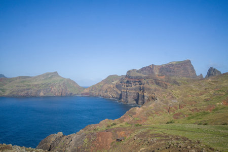 Bright sunlight illuminates the dramatic cliffs of Ponta de Sao Lourenco in Madeira, framing the tranquil blue ocean and lush greenery, perfect for outdoor enthusiasts seeking adventure.の写真素材