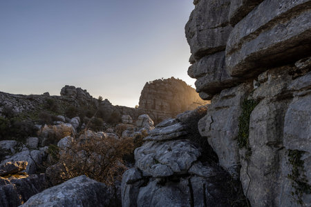 Sunlight breaks over the rocky landscape of El Torcal in Spain. Unique stone formations are visible...