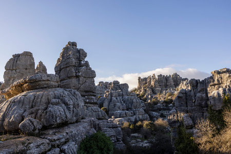 Visitors walk among the large stone structures of El Torcal in Spain. The sun shines on the rocks,...