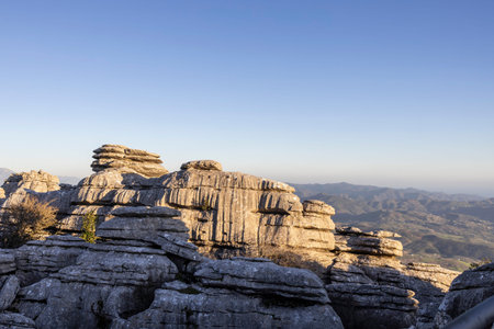 Visitors explore the unique rock formations of El Torcal in Spain. The sun sets, casting light on the landscape while mountains are visible in the distance.の写真素材