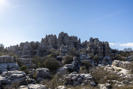 Groups walk among large limestone rocks in El Torcal, Spain. Bright blue sky fills the backdrop...
