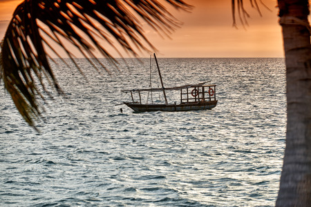 Typical dhow and palm leaf swings in sea at sunset, Zanzibar, Tanzania, Africaの写真素材