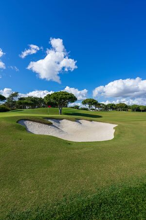 Beautiful, empty golf course with blue sky and green grass with tree and hazardの写真素材