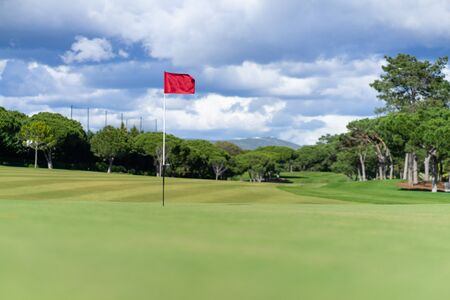 Beautiful golf course in summer with red golf flag and green grassの写真素材