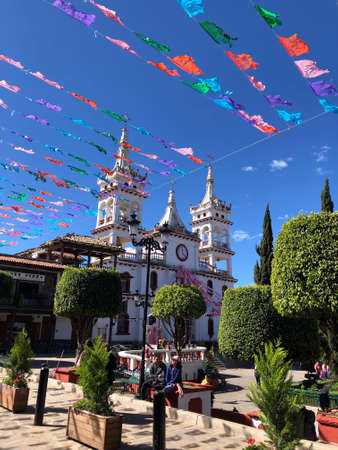 Church in Mazamitla, Mexico with ornamets, lamps, trees and blue sky with a couple sitting in a benchのeditorial素材
