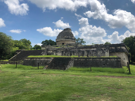 The Observatory pyramid in Chichen Itza, Yucatan, Mexico with a blue sky and some clouds and green...