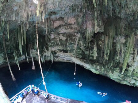 Cenote in Yucatan, Mexico with people swimming in blue clean water and a lot of stalacmites and stalactitesの写真素材
